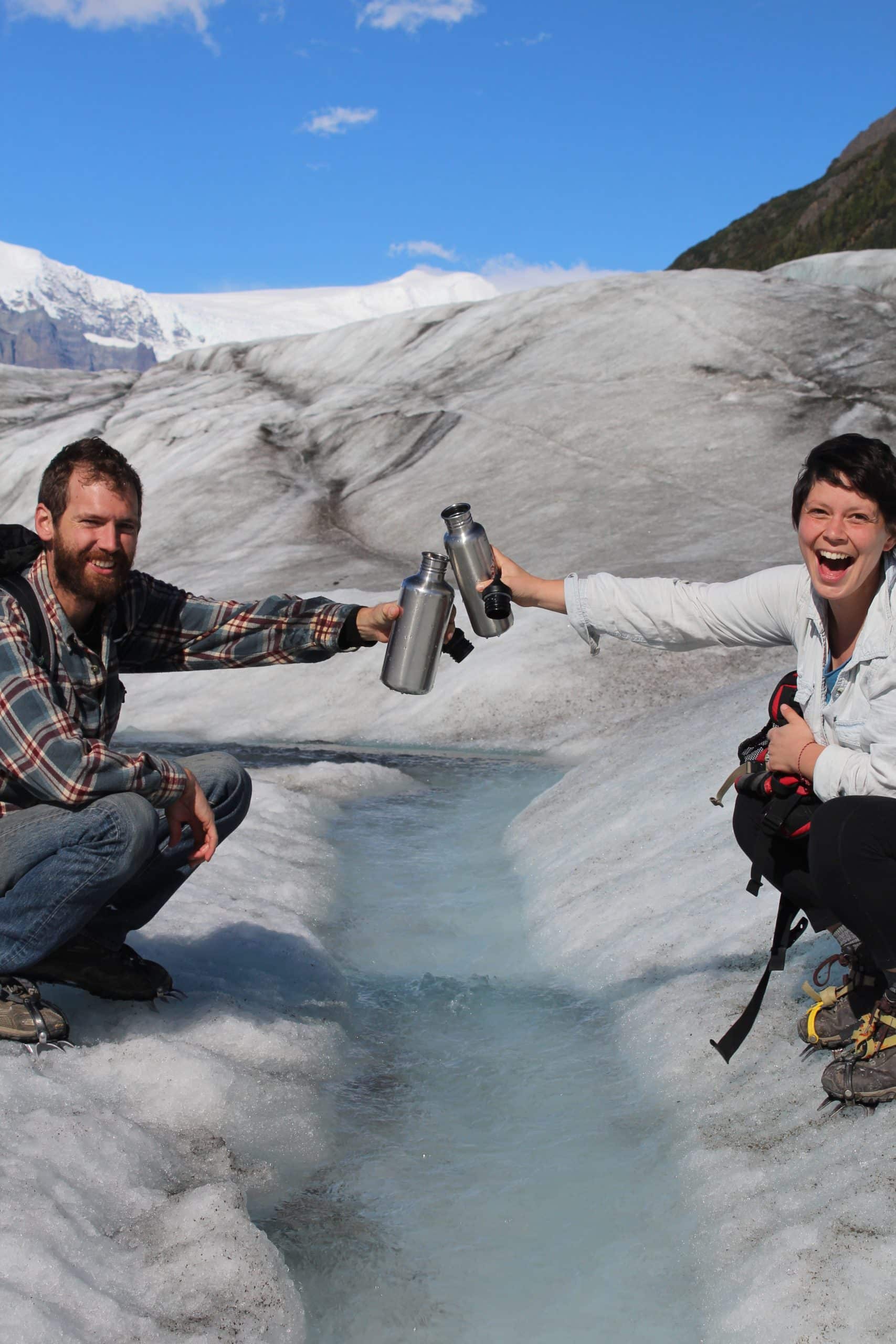 Two people cheers with water on the glacier